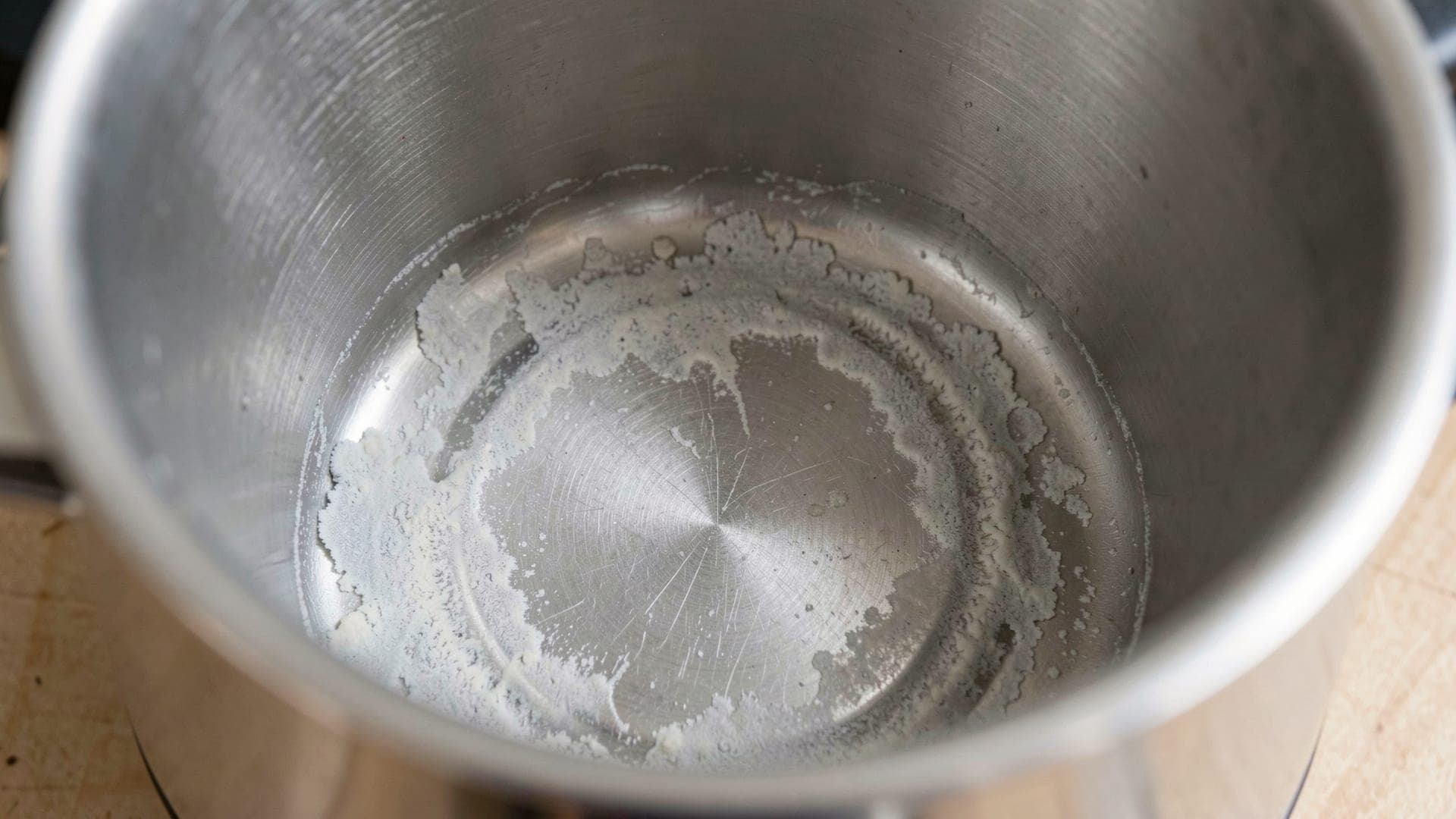 Looking down into a steel kettle with a pale chalky crust of limescale coating the bottom and the heating plate